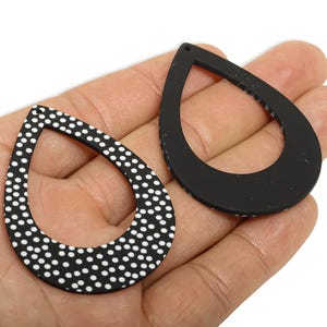 May include: Two black teardrop-shaped pendants. One has a white polka dot pattern, the other is solid black. The pendants are open in the centre and have a small hole at the top for hanging. These are likely jewellery components.