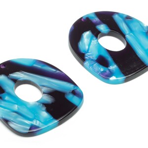 May include: Two abstract teardrop-shaped pendants with a hole in the center. The pendants feature a marbled pattern of blue, purple, and black. These could be used as jewelry components or decorative elements.