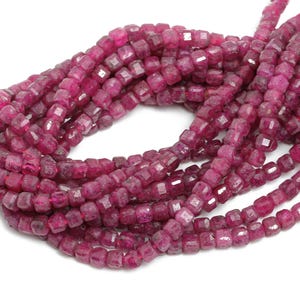 May include: A strand of pink ruby beads, each bead is faceted and has a square shape.