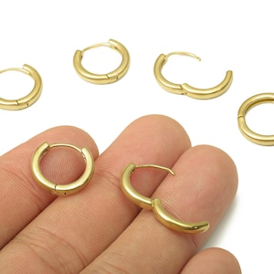 May include: Gold-colored hoop earrings in various sizes are displayed against a white background. Some earrings are open, showcasing the clasp mechanism. The earrings are small and circular, suitable for everyday wear.