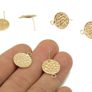 May include: Gold-colored, hammered-texture stud earring components. The earrings have a circular design with a textured surface and a loop for attaching additional elements. The posts are visible, and the earrings are shown in various angles.