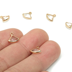 May include: Gold-toned metal charms with a fan-like shape and a clear, faceted center. The charms have a small loop at the top for attaching to jewelry. Several charms are scattered on a white background.