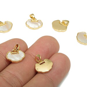 May include: Gold-colored pendants with a mother-of-pearl inlay. The pendants have a unique, irregular shape and a small loop for attaching to a chain or other jewelry. Several pendants are scattered on a white background.