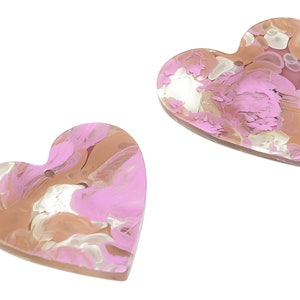 Może przedstawiać: Dwa sercowate ozdoby z żywicy w kolorze różowym i brązowym z marmurowym wzorem.