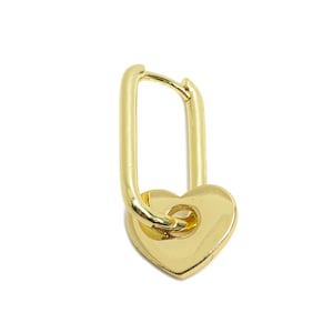 Puede incluir: Un charm de color dorado en forma de corazón con un bucle en la parte superior. El charm está unido a un anillo de metal dorado.