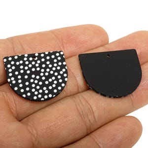 May include: Two black and white half-circle pendants. One has a white polka dot pattern on a black background. The other is solid black. Both have a small hole at the top for stringing, suitable for jewellery making.