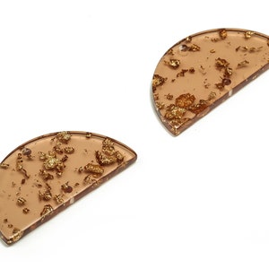 Może przedstawiać: Dwa półkoliste kawałki żywicy z wtopionymi złotymi płatkami w przezroczystej żywicy. Żywica jest jasnobrązowa.