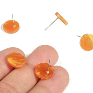 May include: Orange and yellow marbled stud earrings. The earrings are round with a post backing. The earrings are made of a translucent material. The earrings are shown on a white background.