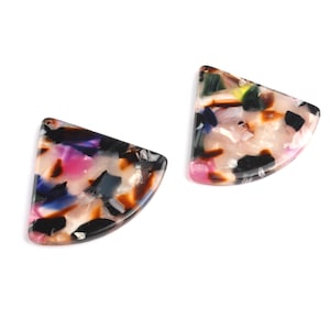 May include: Two abstract, semi-circular shaped acrylic beads. The beads have a marbled pattern with pink, black, blue, and brown colors. The beads are set against a white background.