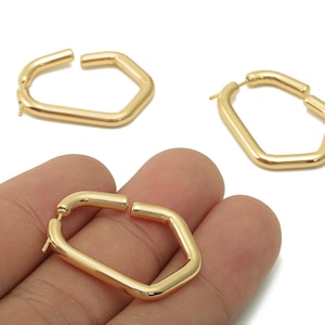 Può includere: Orecchini a cerchio geometrici color oro. Gli orecchini hanno un design angolare unico, con una forma esagonale. Un orecchino è tenuto in mano, mentre altri due sono esposti separatamente. Gli orecchini sono realizzati in un materiale metallico lucido.