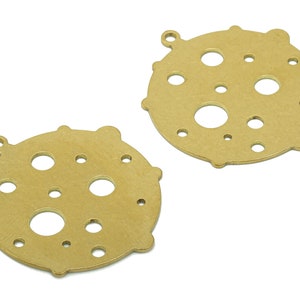 Puede incluir: Dos abalorios de metal de color dorado con forma de círculo con múltiples agujeros pequeños recortados. Los abalorios tienen un bucle en la parte superior para sujetarlos a un collar o una pulsera.