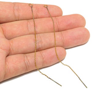 May include: A pair of delicate gold-colored chain earrings. Each earring features a thin chain with a small loop at the top and a straight bar at the bottom. The earrings are displayed against a light background.