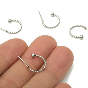 May include: Silver-toned hoop earrings with a twisted rope design. Each earring features a small ball at the end of the hoop. The earrings are displayed against a white background.