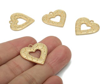 May include: Gold-colored heart-shaped charms with a textured surface and a heart-shaped cutout in the center. The charms have a small loop at the top for attaching to jewelry. The image shows several charms, with one held in a hand.