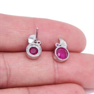 May include: A pair of silver stud earrings with a round, deep red gemstone center. Each earring has a small, fan-shaped accent and a post for pierced ears. The gemstones are a vibrant, eye-catching color.