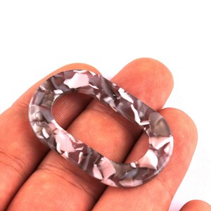 Peut inclure: Un maillon ovale en acrylique dans les tons de gris, rose et blanc. Le motif marbré crée un design unique. Ce maillon décoratif est idéal pour la fabrication de bijoux ou les projets d'artisanat.