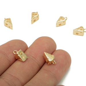 Peut inclure: Pendentifs en forme de fromage de couleur or. Chaque breloque a la forme d'une part de fromage avec des trous et une petite boucle pour l'attacher à des bijoux. Les breloques sont présentées sur fond blanc.