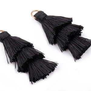 May include: Two black tassel trims with three layers of fringe. The tassels are attached to gold rings.
