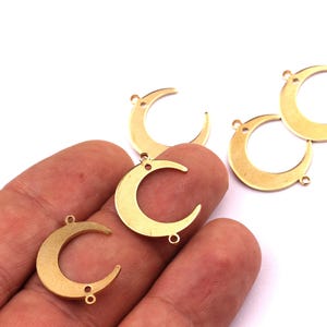 May include: Gold-coloured crescent moon charms with small loops for jewellery making. The charms are in various positions, with one held in a hand. The charms are made of a shiny, metallic material.