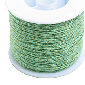 May include: A spool of teal and gold thread. The thread is wound tightly around the spool, which is white and has a smooth surface.