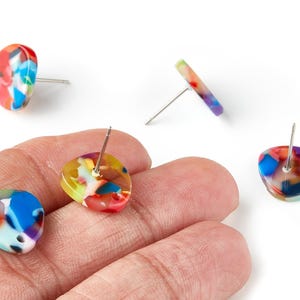 Puede incluir: Pendientes de botón de resina colorida con un patrón de mosaico de rojo, azul, amarillo y blanco. Los pendientes tienen un cierre de poste y se muestran sobre un fondo blanco.