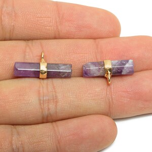 May include: Two amethyst gemstone pendants with gold-colored metal accents. The rectangular gemstones are a mix of purple and white. Each pendant has a small loop for attaching to a chain or other jewelry component.
