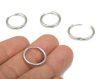 Könnte beinhalten: Silberfarbene Creolen. Die Ohrringe sind kreisförmig und haben einen Klappverschluss. Ein Ohrring ist geöffnet, die anderen sind geschlossen. Die Ohrringe sind vor weißem Hintergrund.