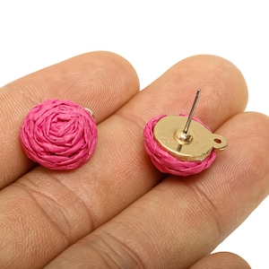 May include: A pair of pink raffia rose-shaped stud earrings. The earrings have a gold-coloured base and post. One earring is shown with the post and back, the other without.