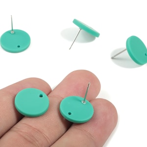 May include: A collection of teal-colored, round stud earrings. Each earring features a post for piercing and a small hole. The earrings are displayed on a white background, with some held in a hand.