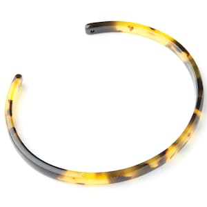 Può includere: Un braccialetto in plastica effetto tartaruga. Il braccialetto è una fascia semplice e sottile con una finitura liscia.