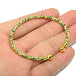 May include: A multi-coloured braided bracelet with gold-coloured end caps. The bracelet has a pattern of green, yellow, red, and white threads. The bracelet is open and flexible.