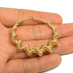 May include: Gold-colored hoop earrings with a unique spiral design. The earrings are made of a shiny, metallic material and feature a clasp closure. The spiral design adds a modern and stylish touch to the jewelry.
