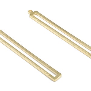 Puede incluir: Dos colgantes rectangulares de metal dorado con superficie texturizada y un bucle en la parte superior.