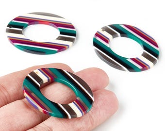 May include: Three oval-shaped resin beads with a striped pattern in teal, white, brown, purple, and black. Each bead has a hole for stringing. The beads are shown against a white background.