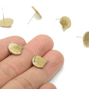 May include: Gold-colored seashell stud earrings. The earrings have a detailed, ridged design, and a post for pierced ears. The earrings are small and delicate, with a loop at the bottom of the shell.