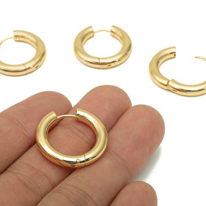 Peut inclure: Quatre boucles d'oreilles créoles dorées. Une boucle d'oreille est ouverte, révélant le fermoir. Les trois autres boucles d'oreilles sont fermées. Les boucles d'oreilles sont épaisses et ont une surface lisse et brillante.