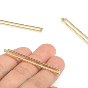 Op de afbeelding: Goudkleurige rechthoekige bedelhangers met een rechthoekige uitsparing in het midden. De bedels hebben een kleine lus aan de bovenkant om aan sieraden te bevestigen. De bedels worden op een witte achtergrond getoond.