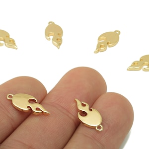 Peut inclure: Charm en forme de flamme de couleur or, avec des boucles pour la fabrication de bijoux. Les breloques ont une finition lisse et polie. Plusieurs breloques sont éparpillées sur un fond blanc.