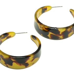 May include: A pair of large hoop earrings with a tortoiseshell pattern. The earrings are made of a thick, glossy plastic and have a brown and yellow color scheme.