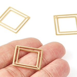 May include: Three gold-colored, open-frame square charms. One charm is held in a hand, while two others are scattered on a white background. Each charm has a smaller square inside a larger square.