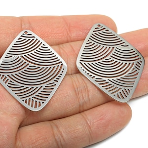 May include: Two silver-colored, diamond-shaped earring pendants. Each pendant features a cut-out design of curved lines, creating a wave-like pattern. The pendants have a small hole at the top for attachment.