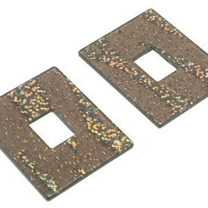 May include: Two brown square-shaped earrings with a smaller square cut-out in the center. The earrings have a glittery, iridescent finish.