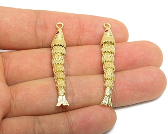 May include: Two gold-colored fish-shaped pendants. Each pendant has a small red gem at the top and a detailed, layered design. The fish have a loop at the top for hanging and a detailed tail.