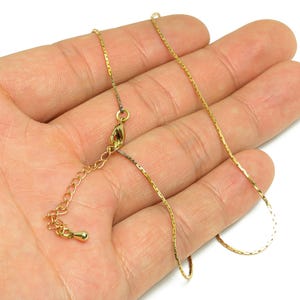 May include: A delicate gold-colored necklace with a thin chain and an adjustable clasp. The necklace is displayed on a hand, showcasing its fine details and elegant design. The chain appears to be approximately 18 inches long.