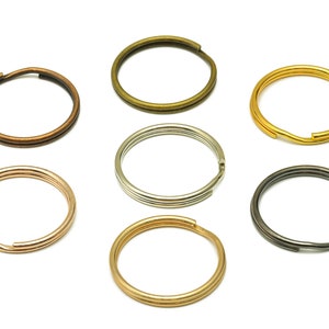 May include: Assortment of seven key rings in different metal finishes: gold, silver, bronze, black, and rose gold. The key rings are all the same size and shape, with a circular design.