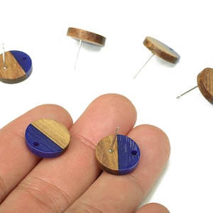May include: Wooden stud earrings with a half-and-half design. One half is natural wood, the other is a deep blue. The earrings have a post for pierced ears. Several earrings are scattered on a white background.