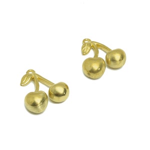 May include: Two gold-colored cherry charms with a leaf detail. The charms are connected by a stem.