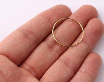 Może przedstawiać: Cienki, złoty metalowy pierścień o średnicy około 2,5 cm spoczywa na dłoni osoby. Pierścień jest okrągły i wydaje się być wykonany z błyszczącego, metalicznego materiału. Tło stanowi gładka, biała powierzchnia.