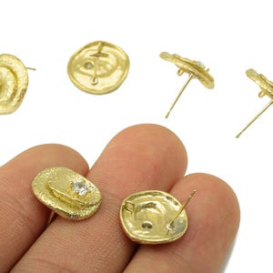 Può includere: Orecchini a lobo color oro con un design strutturato e organico. Ogni orecchino presenta una piccola gemma trasparente. Gli orecchini sono esposti su sfondo bianco.