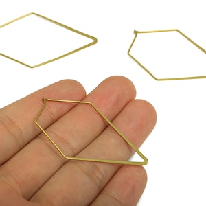 May include: Three gold-colored geometric earring components. One is held in a hand, while two others are displayed separately. The earrings have a unique, angular design, perfect for crafting modern jewelry.